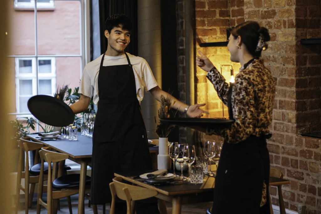 Two smiling waiters are talking while they're setting the tables in the restaurant